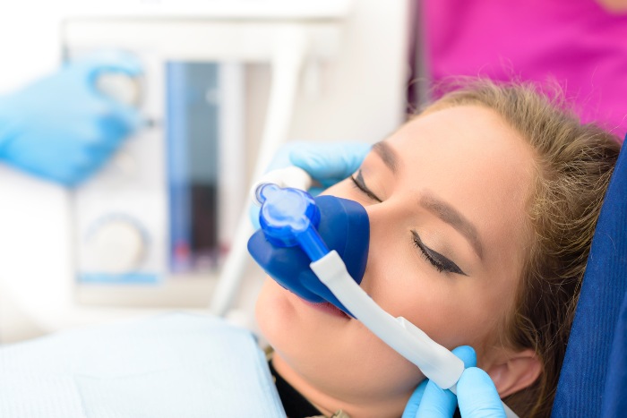 Dental sedation procedure with the patient reclined and gloved hands adjusting equipment in Edmonton