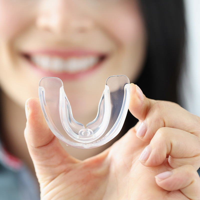Smiling woman holds transparent plastic mouth guard in her hand