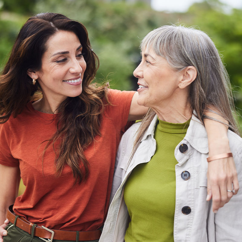 Woman standing arm in arm with her senior mother and smiling