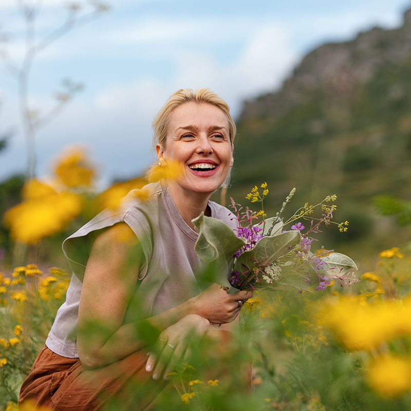 A cheerful woman holding wildflowers sits amidst a beautiful meadow